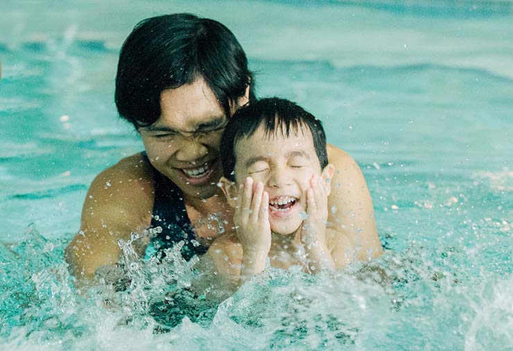 A child with autism and his support worker splash in the water together at our I CAN Swim program.