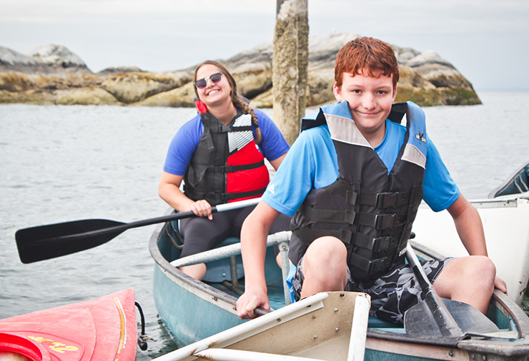 A child with autism and his support worker pose in a canoe together in our Overnight Camp program.