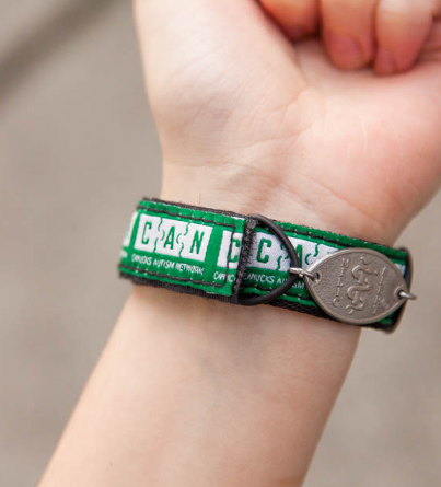 A green MedicAlert Canucks Autism Network bracelet worn on an individual's wrist