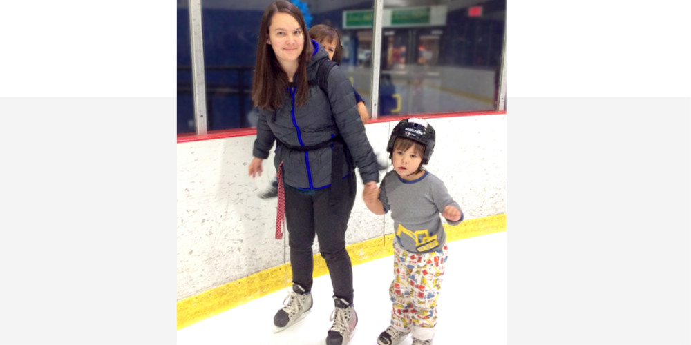 A mother skates on the ice while holding her son's hand.