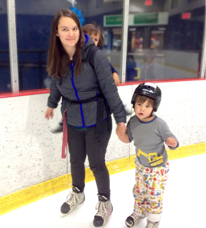 A mother skates on the ice while holding her son's hand.