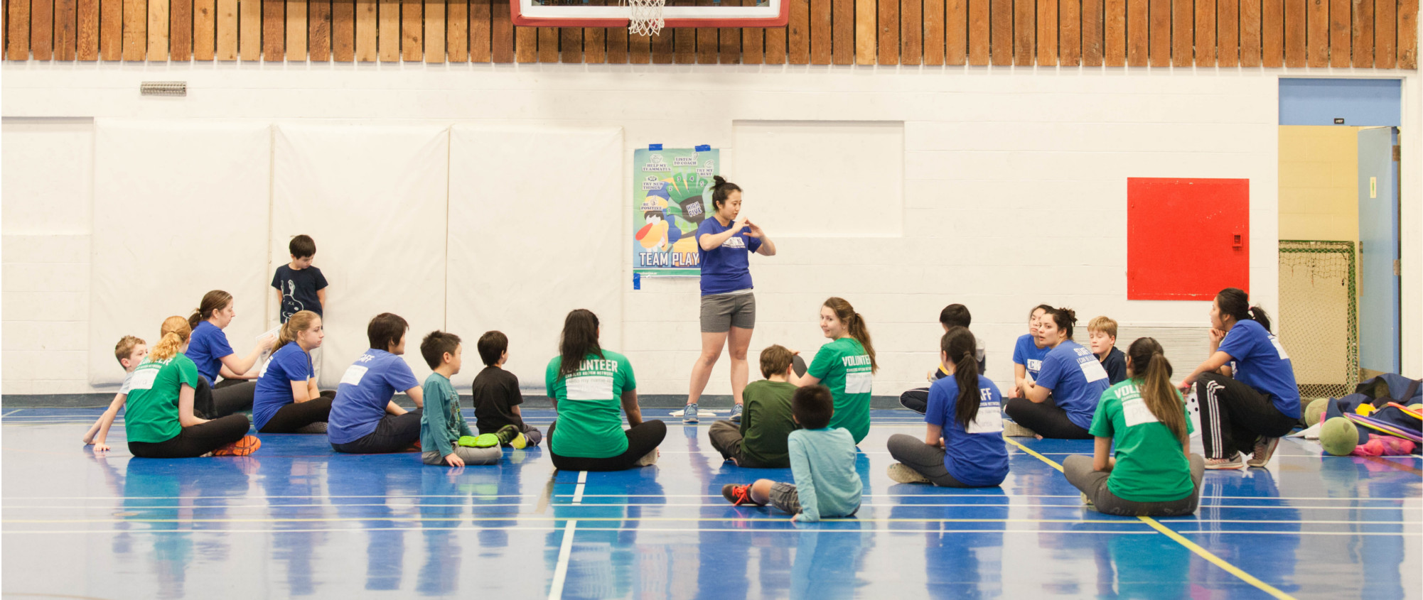 A coach stands in front of seated staff, volunteers and participants within a sports program.