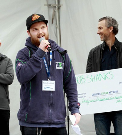 A young man speaks with a microphone with a man standing behind him with a giant cheque.