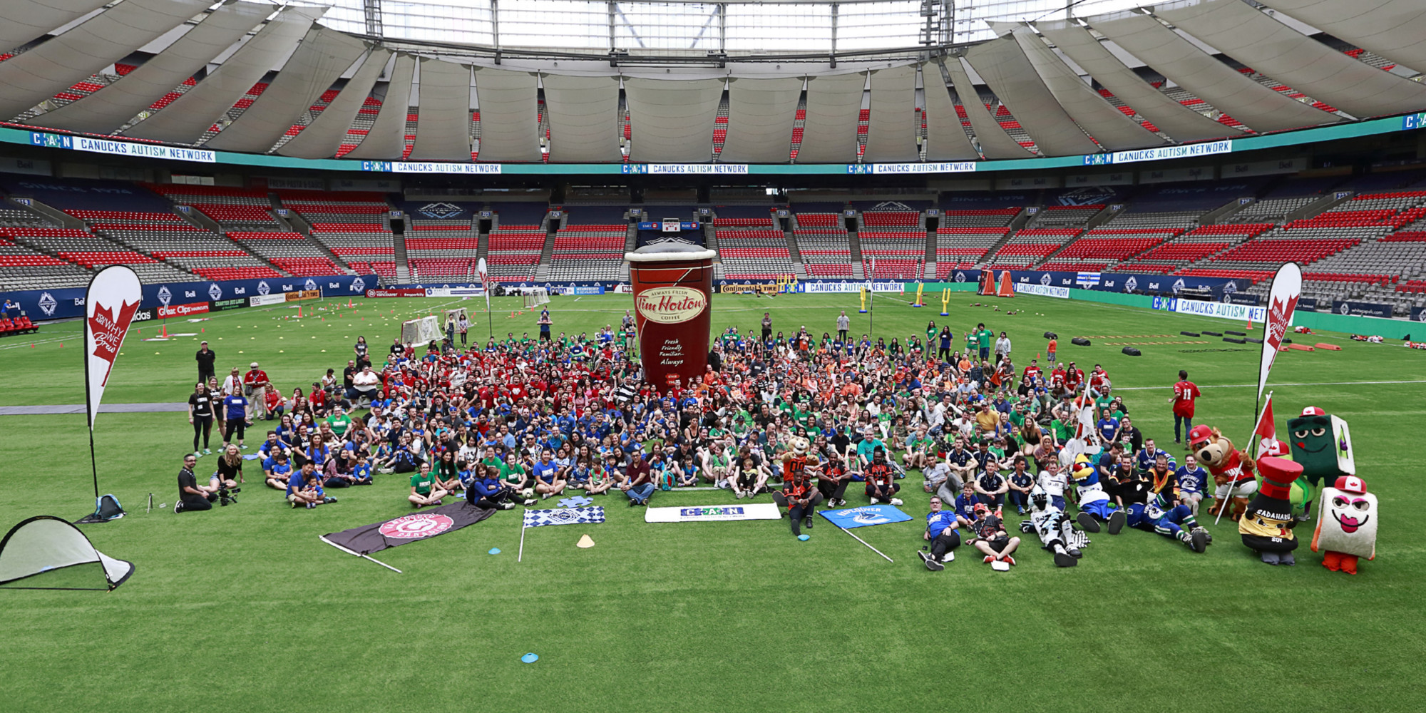A group of 300+ families, staff, volunteers and professional athletes pose for a photo on-field at a sports stadium.