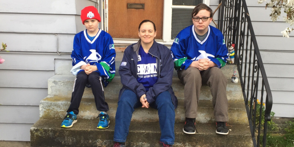 A mother and her two boys sit on their front porch steps wearing hockey jerseys.