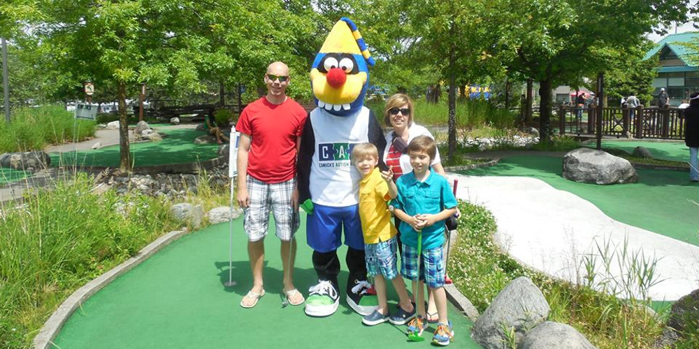 A family of four pose for a photo with a mascot on a mini golf course.