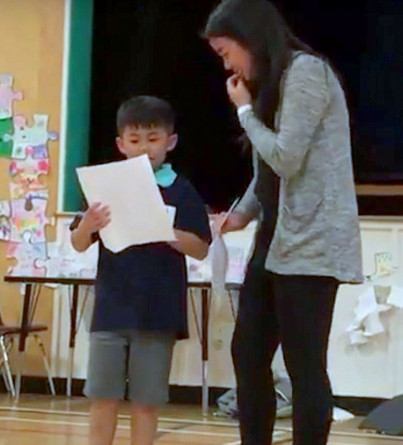 A young boy recites a poem while his older sister watches beside him.